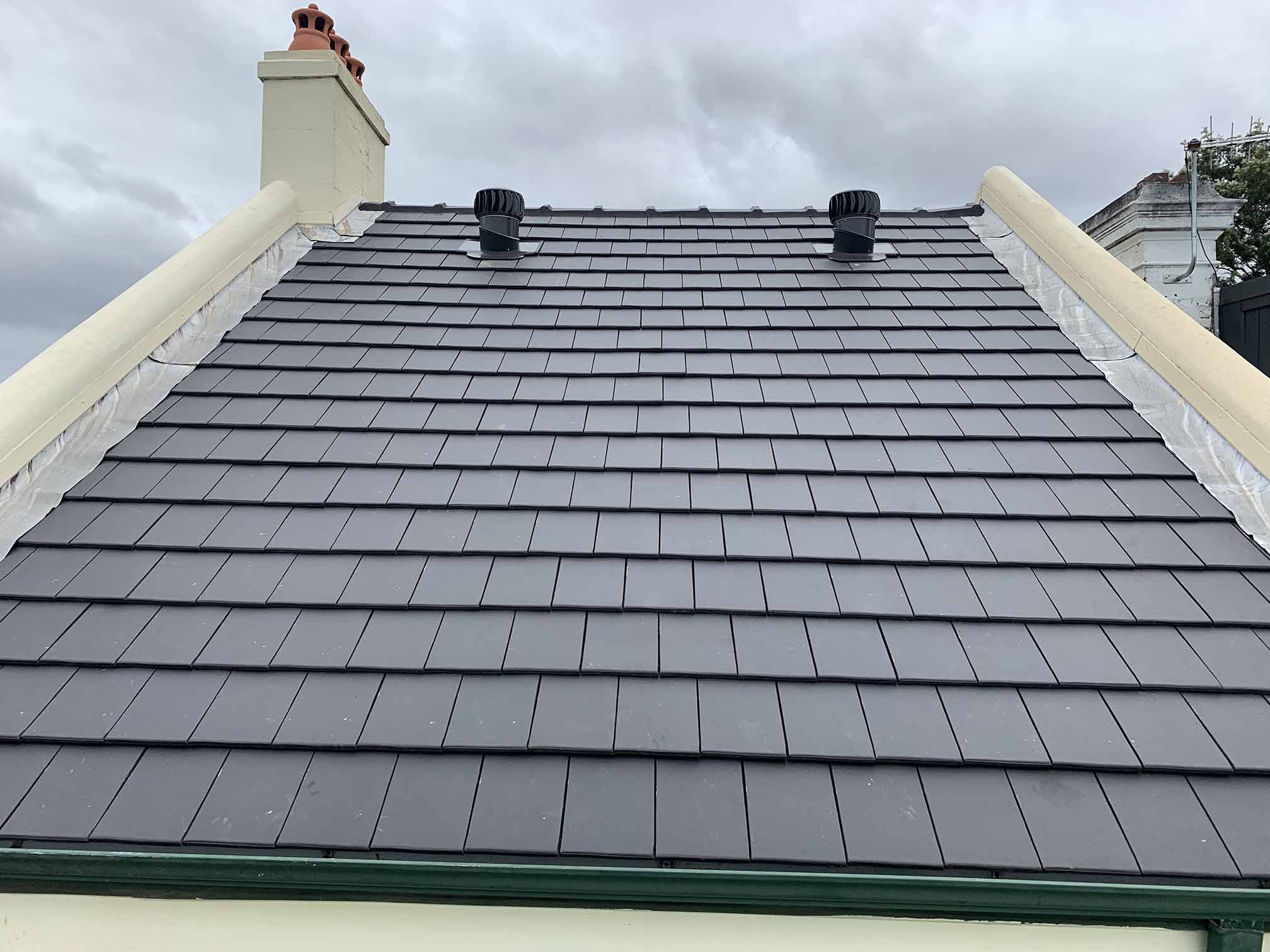 Dark flat-tiled roof with two vents between rendered side walls