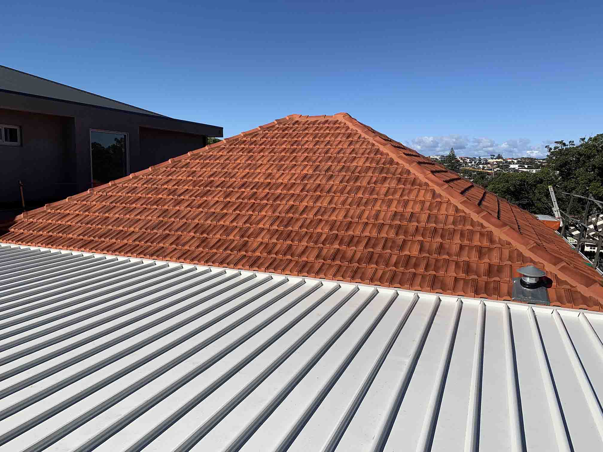 Light grey ribbed metal roof below a terracotta tiled roof