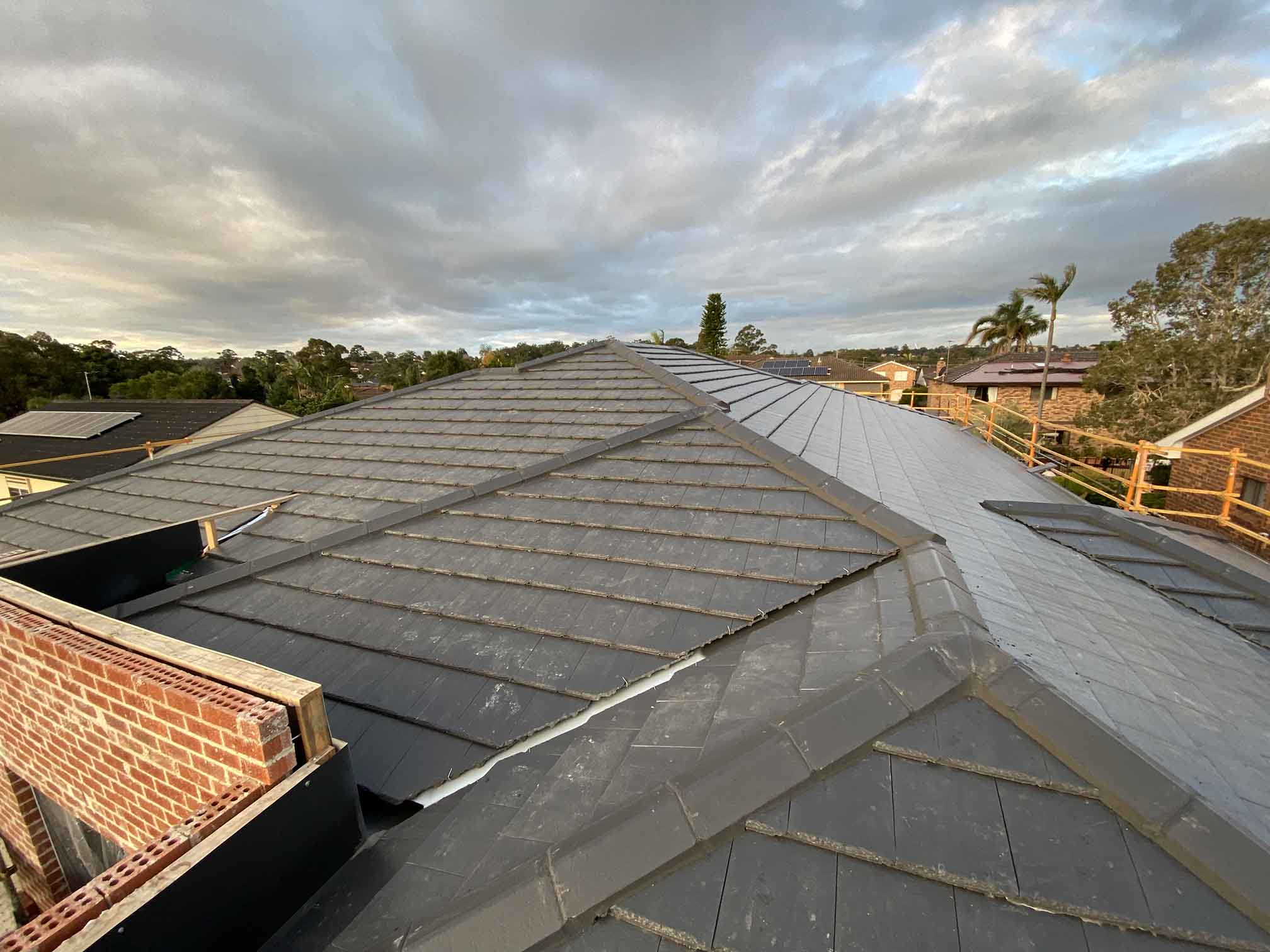 Grey tiled roof beside a brick wall under a cloudy sky