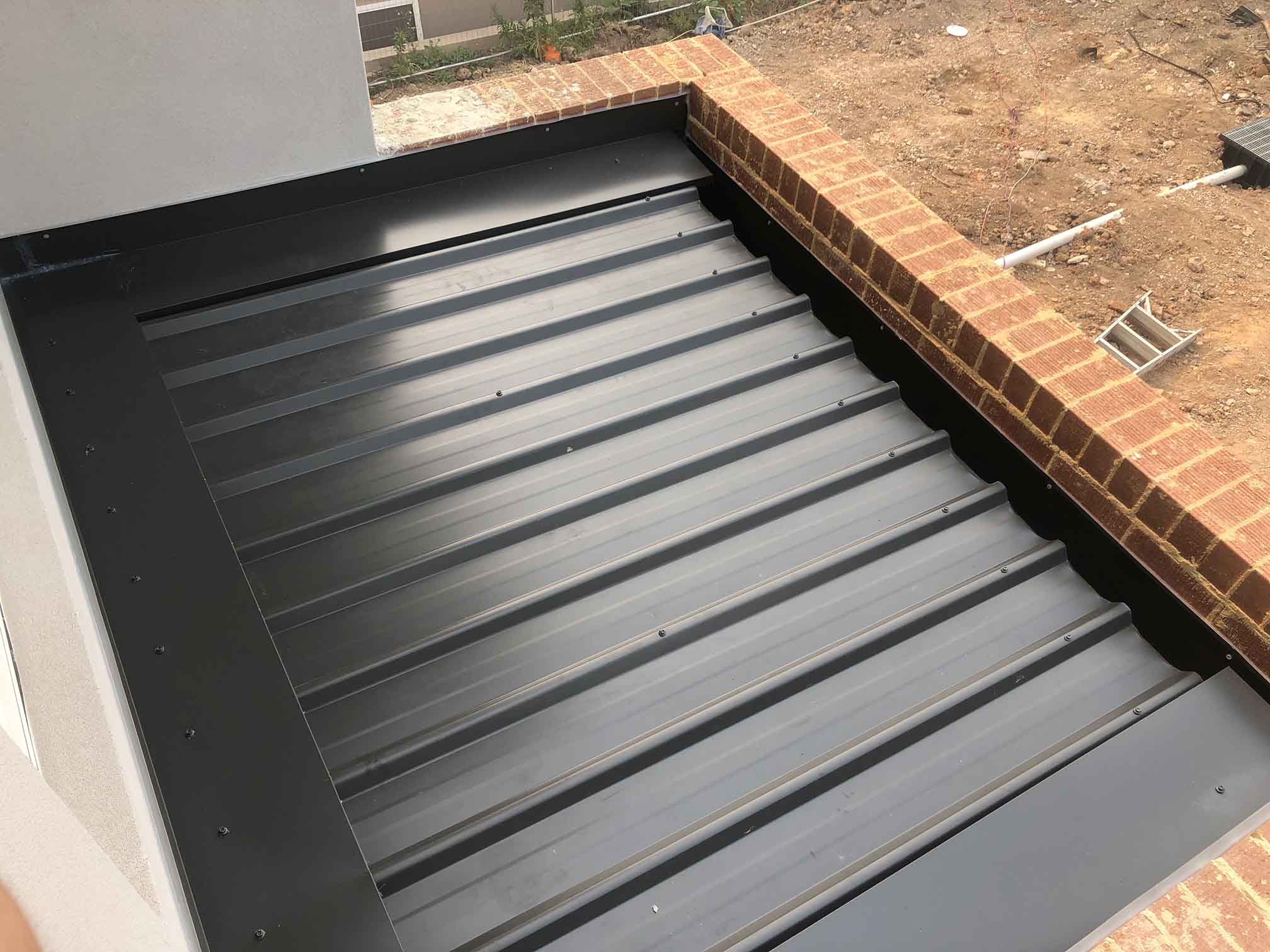 Charcoal metal roof sheets laid against a brick parapet wall