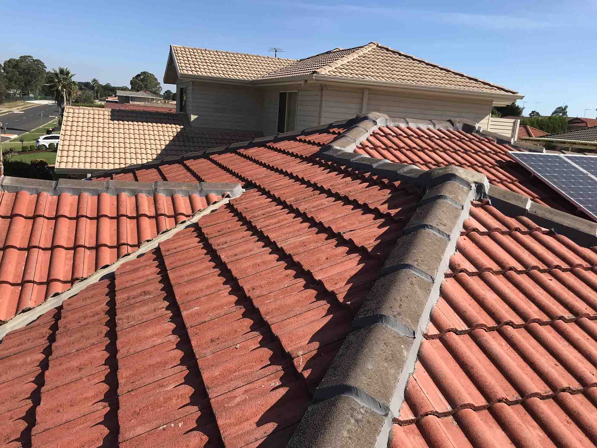 Terracotta tiled roof with grey ridge capping, two-storey house behind