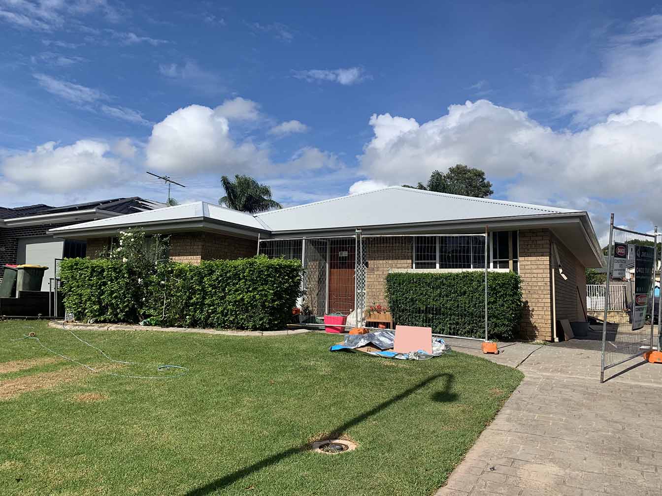 Brick house with a pale grey metal roof behind a front lawn and hedges